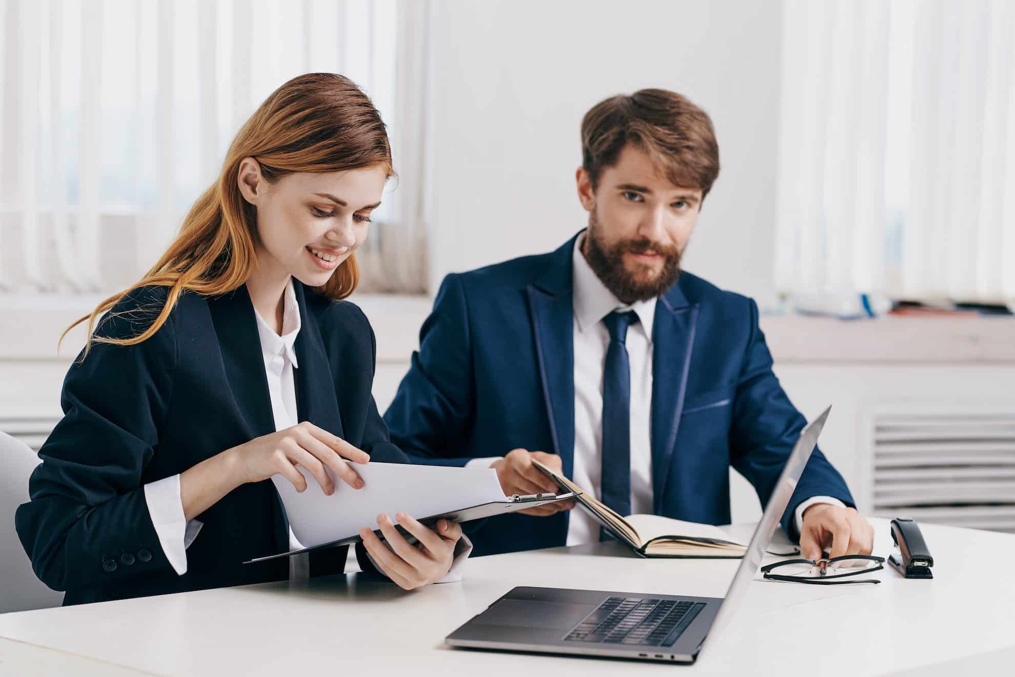 Two business professionals in a formal office setting reviewing paperwork and a laptop, representing preparation for an FTA reconsideration request under UAE Federal Tax Authority procedures.