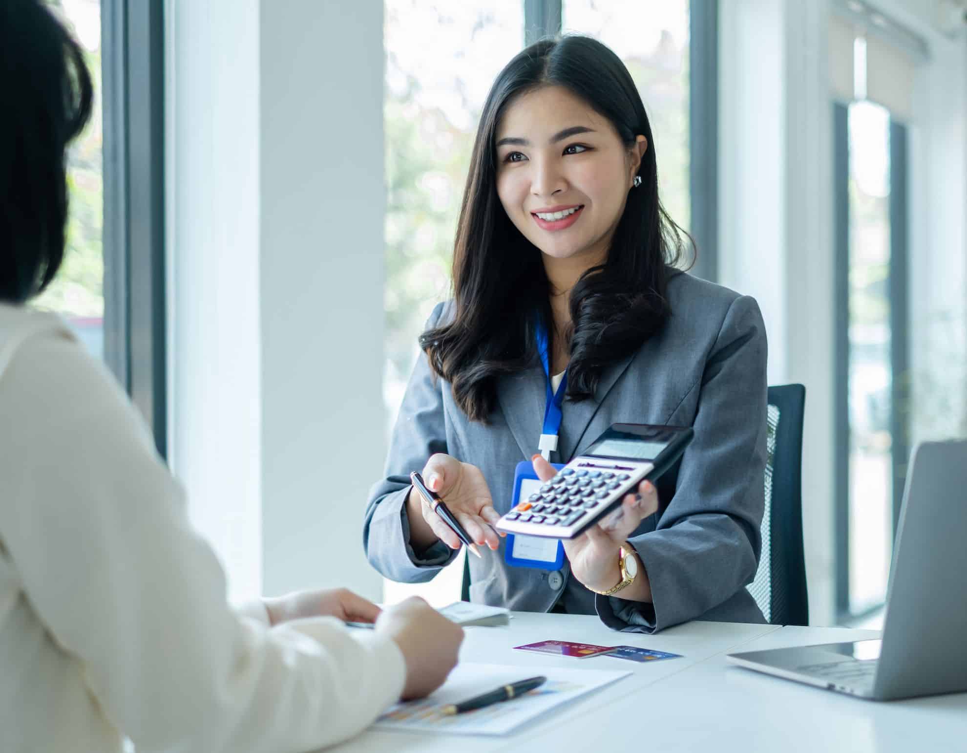 Smiling female professional showing a calculator during a business consultation in an office where she is advising on VAT payment in the UAE.