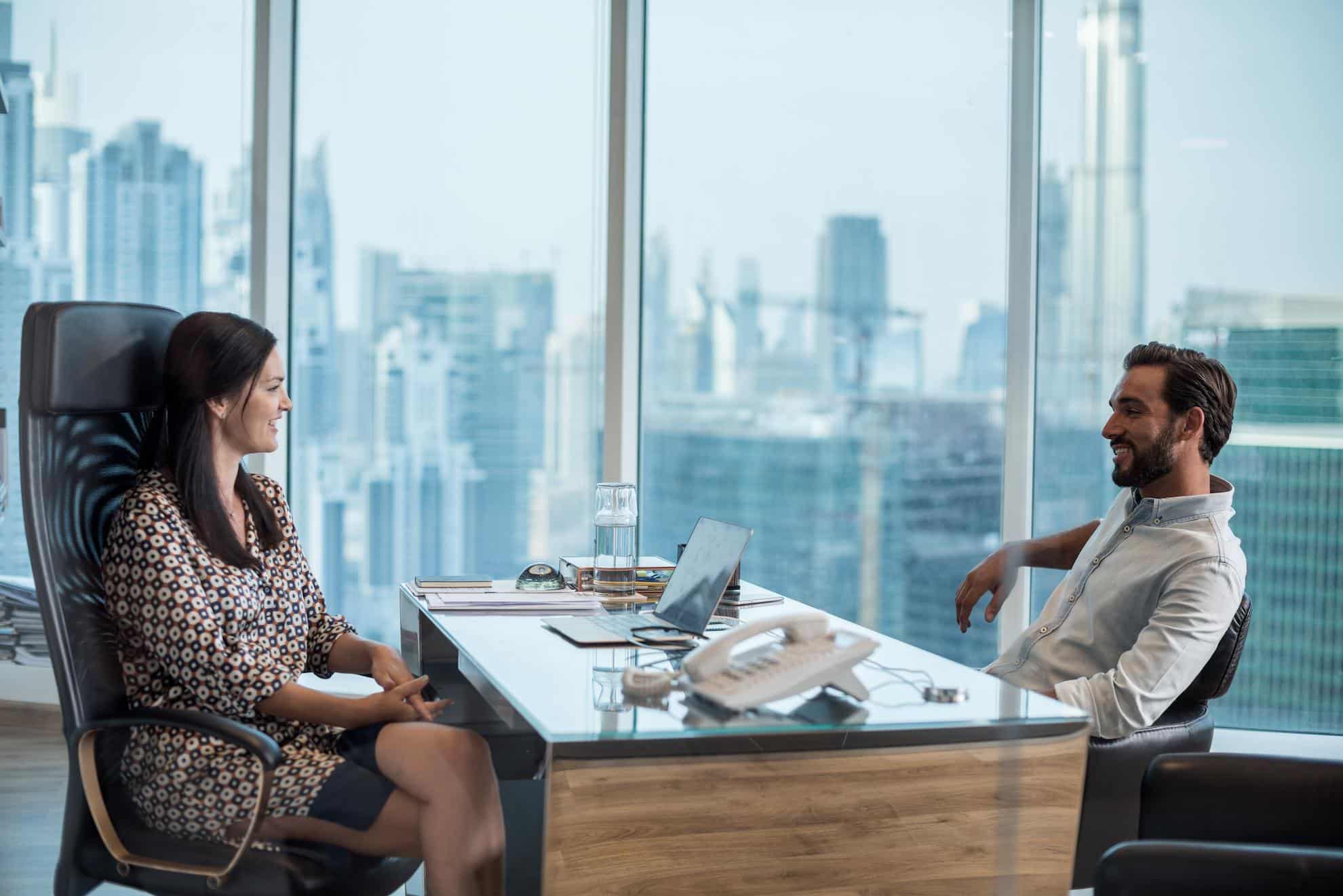 Two business professionals meeting in modern Dubai office with city skyline in background discussing No Objection Certificate requirements in the UAE.