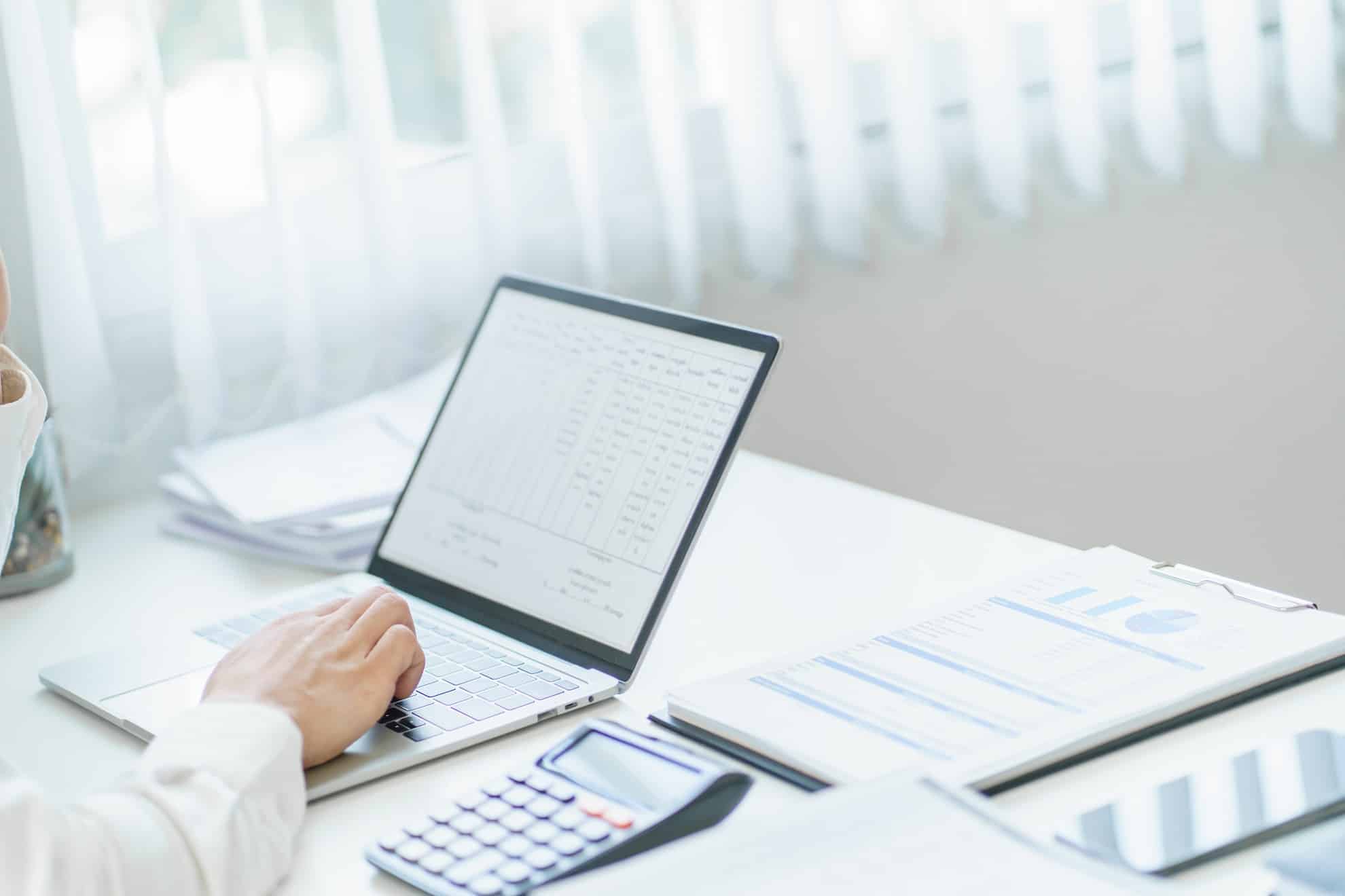 Accountant reviewing tax documents and entering data on laptop for FTA tax clearance and No Objection Certificate in the UAE.